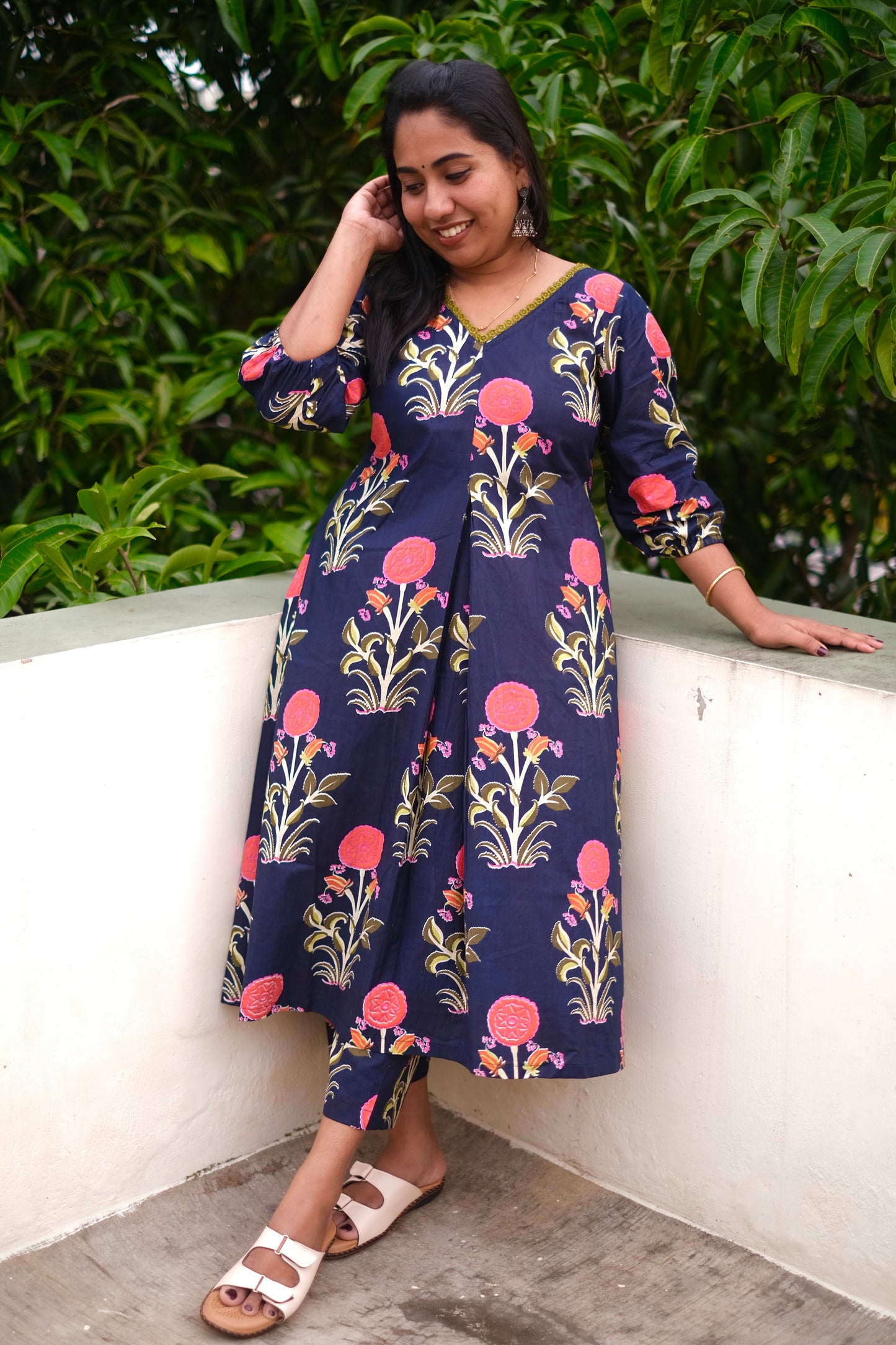 Woman wearing a floral dress with a white wall and greenery in the background