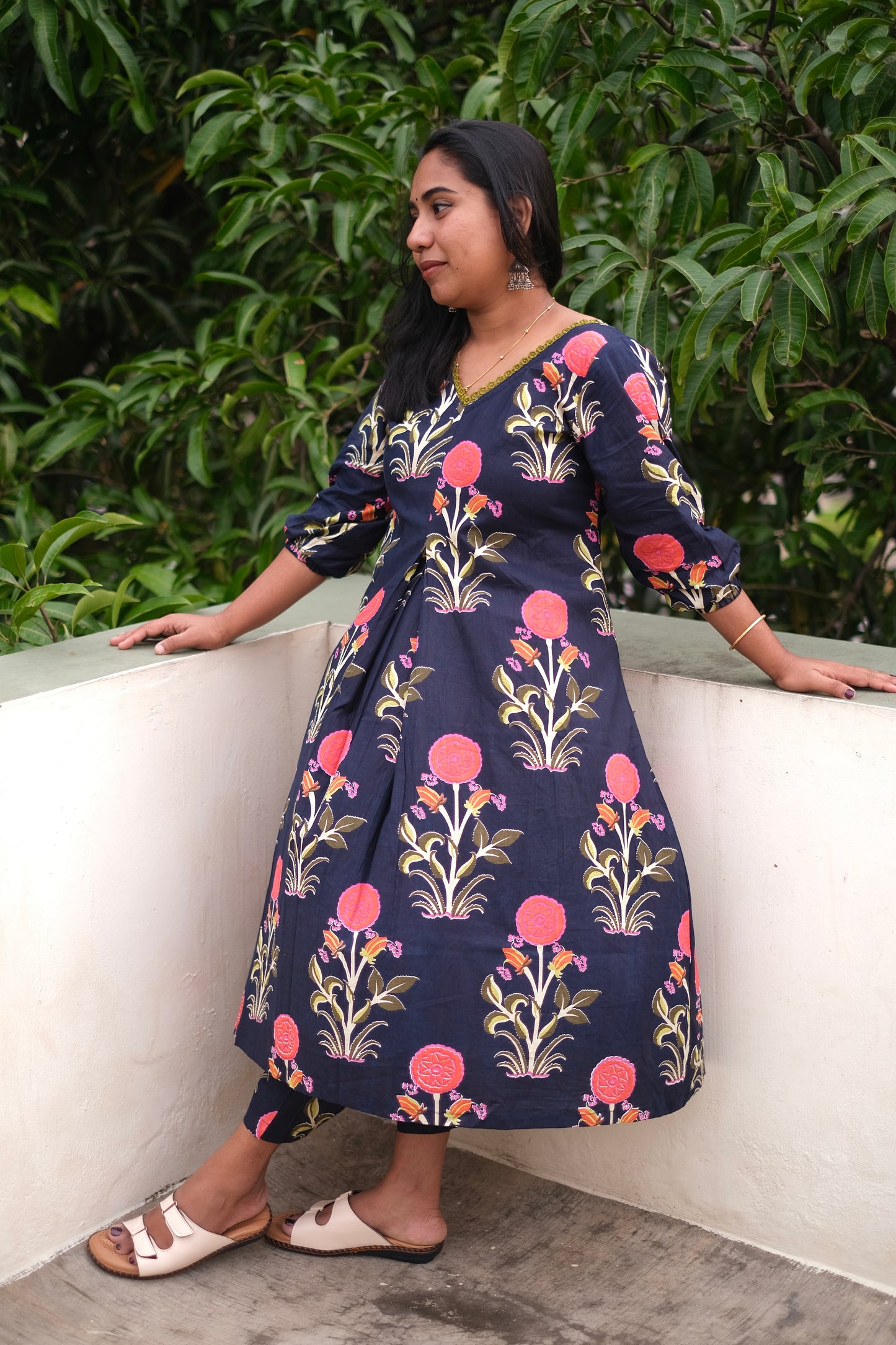 Woman wearing a floral dress sitting on a ledge with greenery in the background